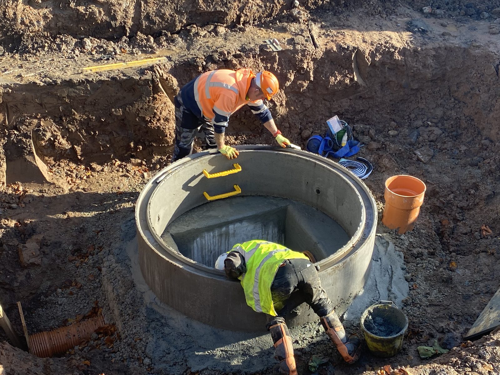 Two operatives constructing a precast concrete manhole chamber in open excavation