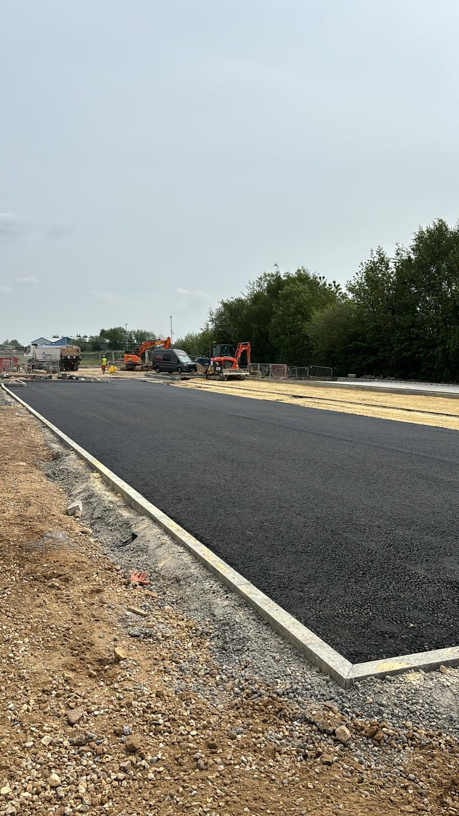 Freshly laid tarmac base course within new kerb lines on an external works area