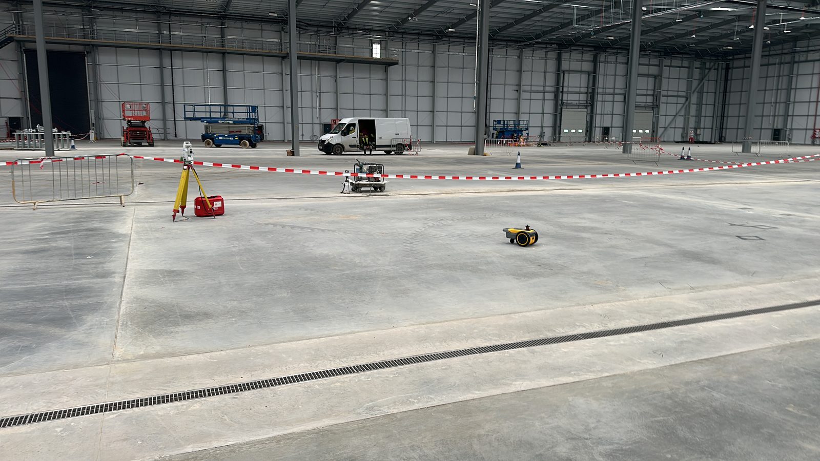 Robotic total station on a tripod surveying a newly poured warehouse floor slab